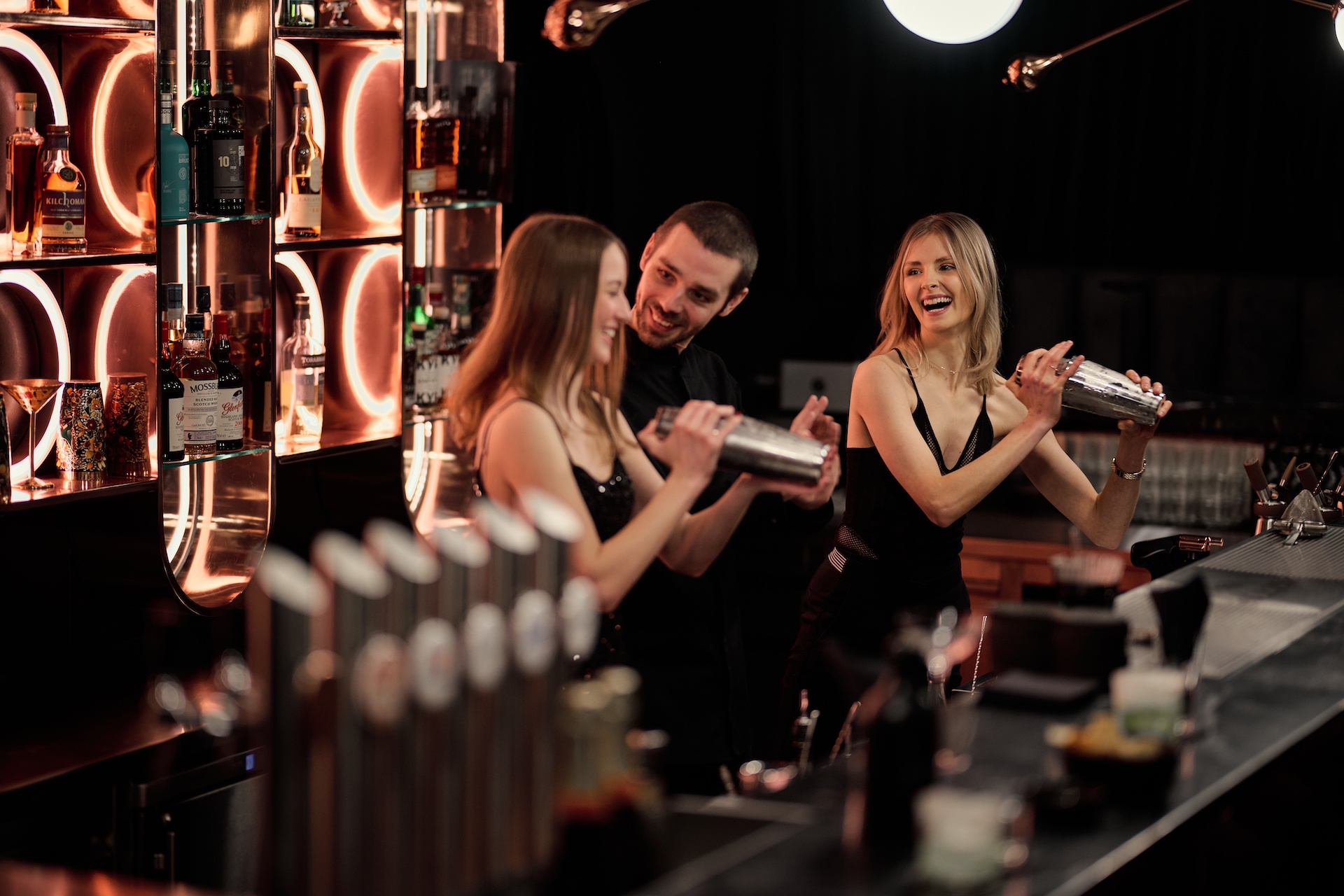Frauen beim Cocktail Shaken gemeinsam mit Barkeeper hinter der Bar